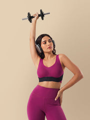 Woman in purple athletic wear lifting a dumbbell against a beige background