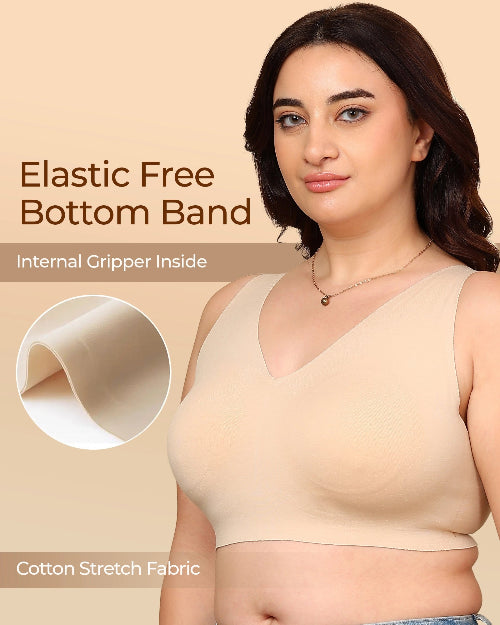 Woman wearing a beige tank top with text about an elastic free bottom band and cotton stretch fabric.