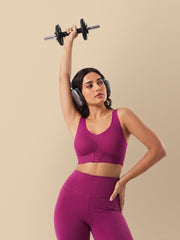 Woman in purple athletic wear lifting a dumbbell against a beige background