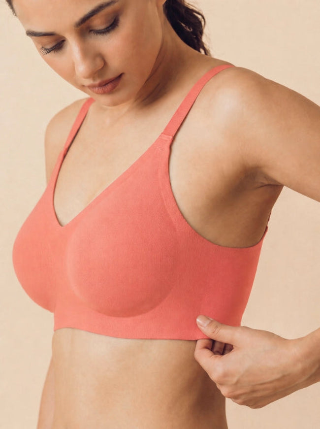 Woman wearing a coral sports bra against a beige background