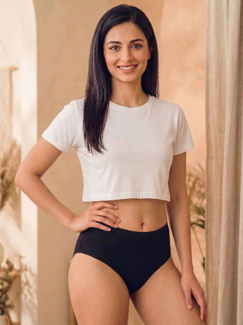 Woman wearing a white crop top and black underwear standing against a neutral background