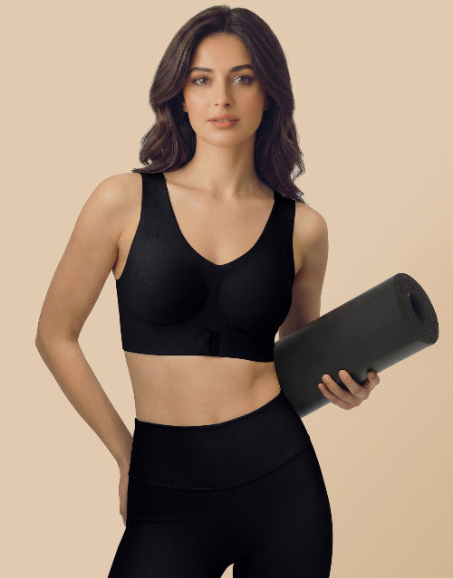 Woman wearing a black sports bra and leggings holding a black yoga mat on a beige background