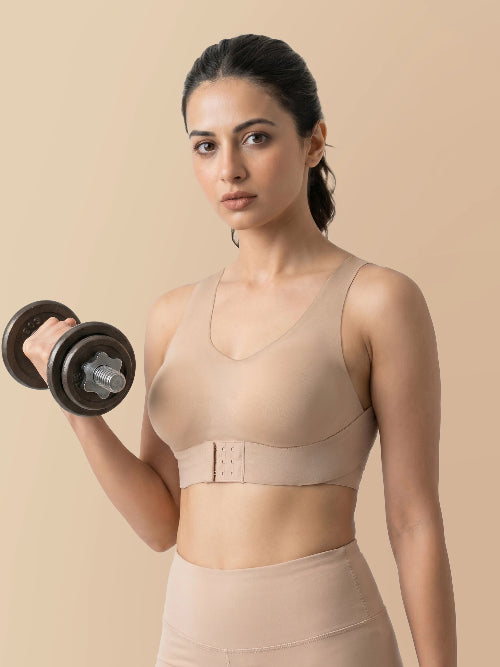 Woman lifting a dumbbell wearing a beige sports bra and leggings on a beige background
